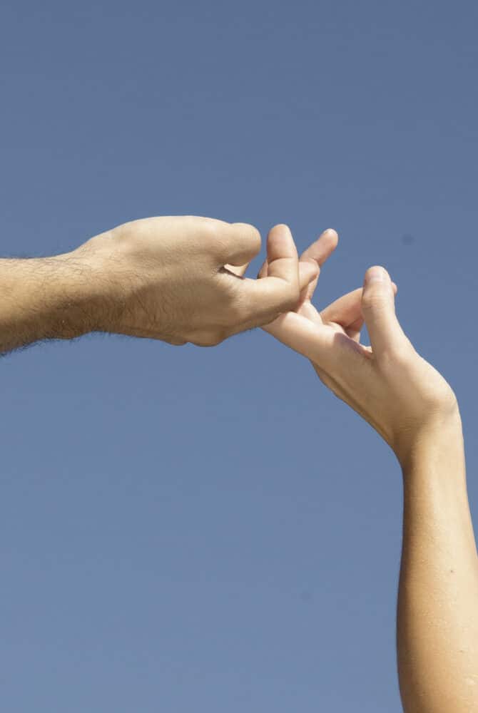two hands held aloft against the sky fingers intertwined